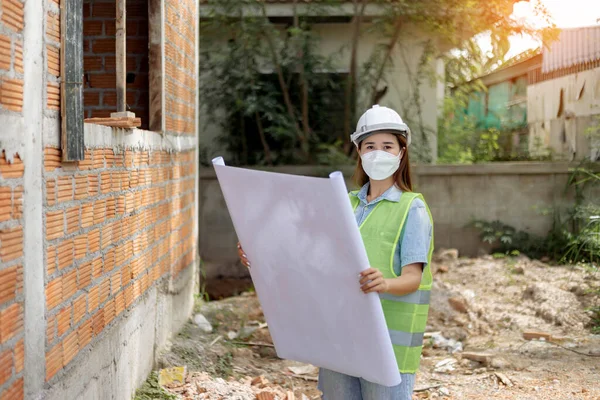 engineer concept The female engineer wearing a white mask and helmet holding her proposal paper of the construction.