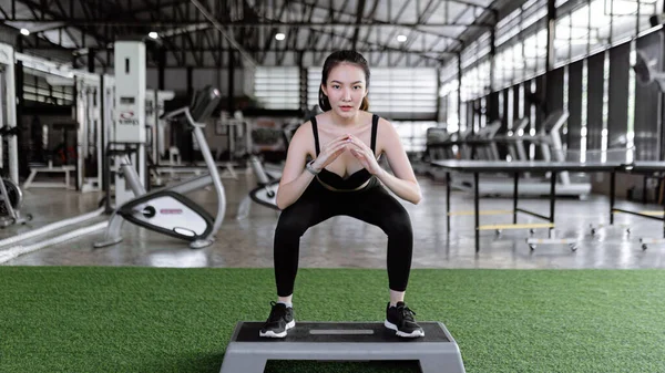 exercise concept The female exercise person doing squats by standing with feet a little wider than hip width, toes facing front on the grey platform.