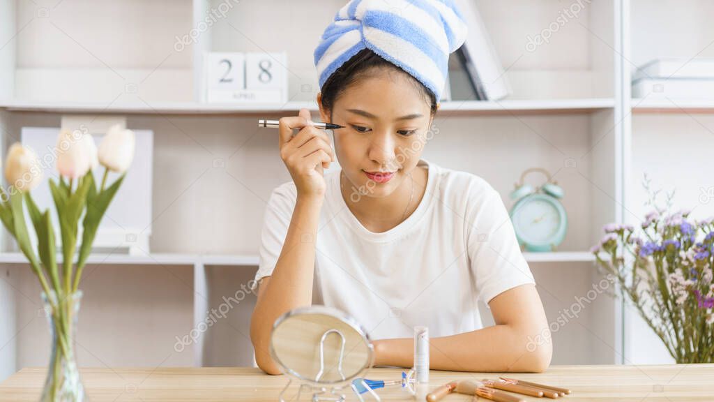 Home relaxation concept, Young woman in turban after shower and apply eyeliner on eyelid for makeup.
