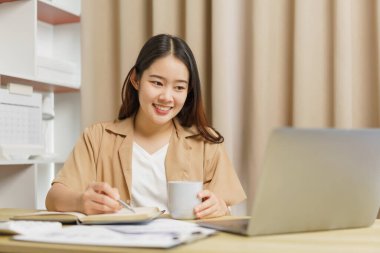 Çevrimiçi yaşam tarzı konsepti. Kadın ev işçisi not defterine kahve fincanı ile sunulan bilgileri yazıyor.