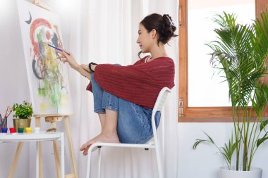 Sanat konsepti, genç Asyalı kadın sandalyeye oturur ve resim çizmek için boya fırçası kullanır..
