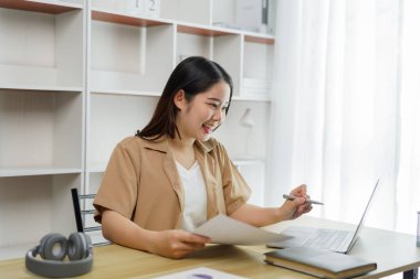 Çevrimiçi yaşam tarzı konsepti: Çalışan bir kadın, kağıt işlerinde ve defterde kaçırdığı ayrıntıları belirtmek için enerjik davranır.