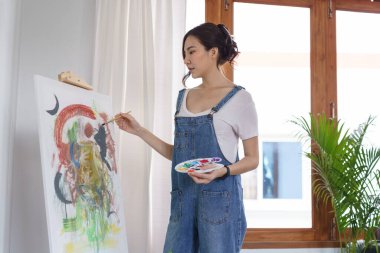 Sanat konsepti, genç Asyalı kadın resim çizmek için renk paletli boya fırçası kullanıyor..