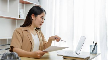 Çevrimiçi yaşam tarzı konsepti: Çalışan bir kadın, kağıt işlerinde ve defterde kaçırdığı ayrıntıları belirtmek için enerjik davranır.