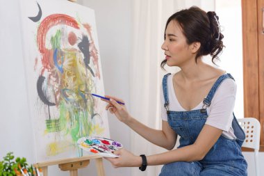 Sanat konsepti, genç Asyalı kadın resim çizmek için renk paletli boya fırçası kullanıyor..