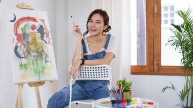 Sanat konsepti, genç Asyalı kadın boya fırçasını tutuyor ve bitirdikten sonra dinlenmek için oturuyor..