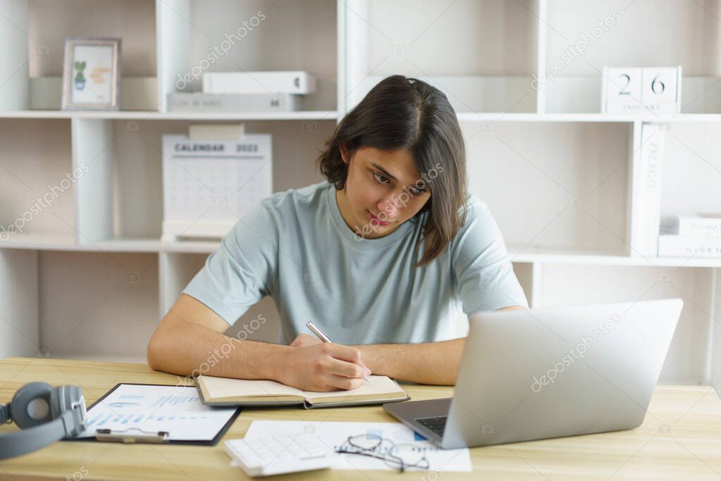 Distance education concept, Teen boy taking notes while studying online with teacher on video call.