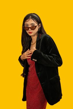 Moda konsepti. Moda kadını, büyük boy siyah ceketle poz vermek için güneş gözlüğü ve kırmızı elbise giyiyor..