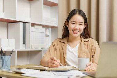 Çevrimiçi yaşam tarzı konsepti. Kadın ev işçisi not defterine kahve fincanı ile sunulan bilgileri yazıyor.