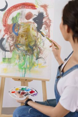 Sanat konsepti yaratıcısı, genç Asyalı kadın stüdyodaki sanat şaheserini boyamak için fırça kullanıyor..