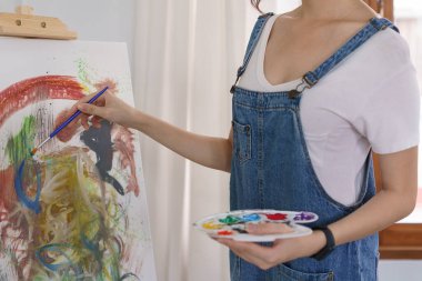 Sanat konsepti, genç Asyalı kadın resim çizmek için renk paletli boya fırçası kullanıyor..