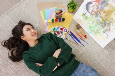 Sanat konsepti, genç Asyalı kadın sanat atölyesinde sanat şaheseriyle yerde yatıyor..