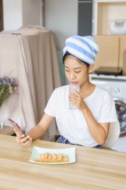 Ev rahatlama konsepti, duş sonrası türbanlı genç bir kadın içme suyu içip sosyal medyada sörf yapıyor..