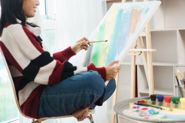 Sanat konsepti, Asyalı kadın ressam sandalyede oturuyor ve resim yapmak için tuval tutuyor..
