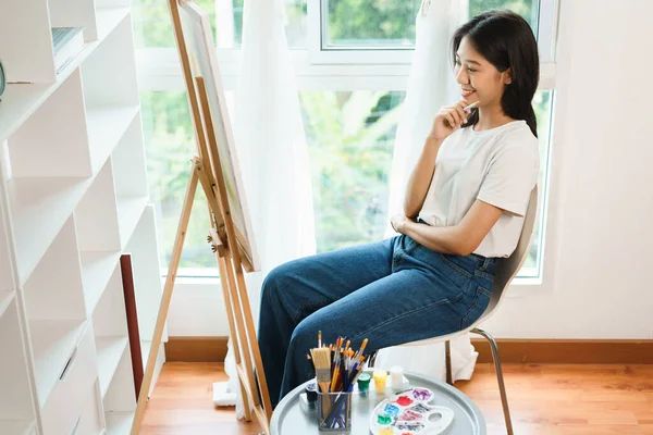 The art concept, Asian female artist sit front of canvas and thinking to create idea for artwork.