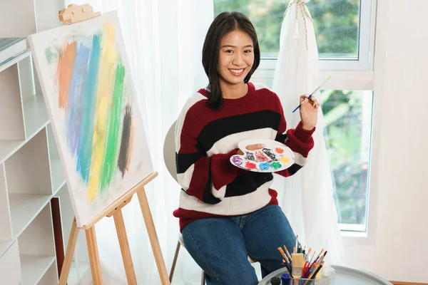 The art concept, Asian female artist holding paint brush and color palette to prepare for painting.