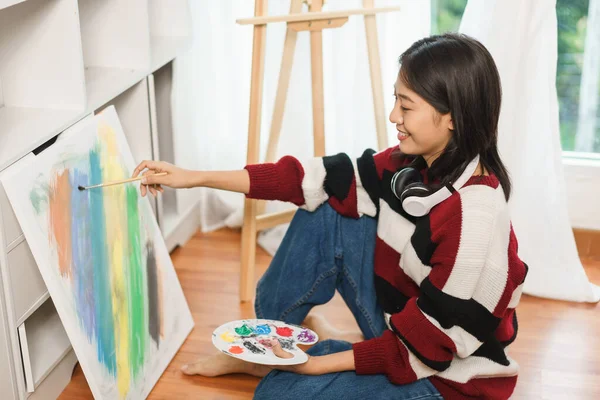 The art concept, Asian female artist sit on the floor and using paint brush to painting on canvas.
