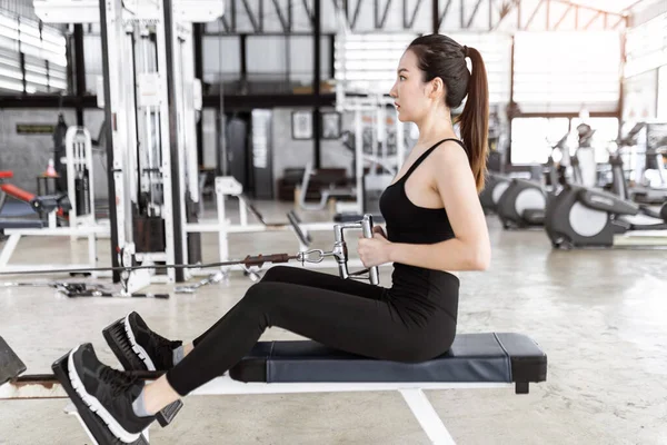 exercise concept The lady wearing sport top, tight pants and black sneakers sitting and concentrating on pulling a flexible rope of seat roll machine.