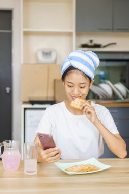 Ev rahatlama konsepti, duş sonrası sarıklı genç kadın kraker yemek ve sosyal medyada sörf yapmak için..