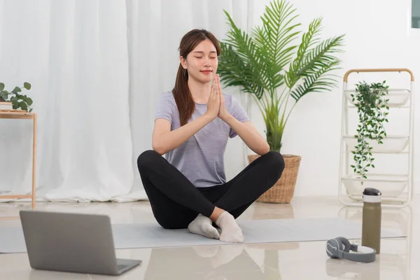 Yoga exercise concept, Young Asian woman in lotus position while doing yoga exercise online at home.