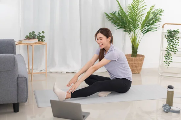 Yoga exercise concept, Young Asian woman is stretching leg and arm while doing yoga online at home.