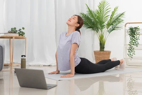 Yoga exercise concept, Asian woman doing yoga with lying in cobra pose and watching tutorial online.