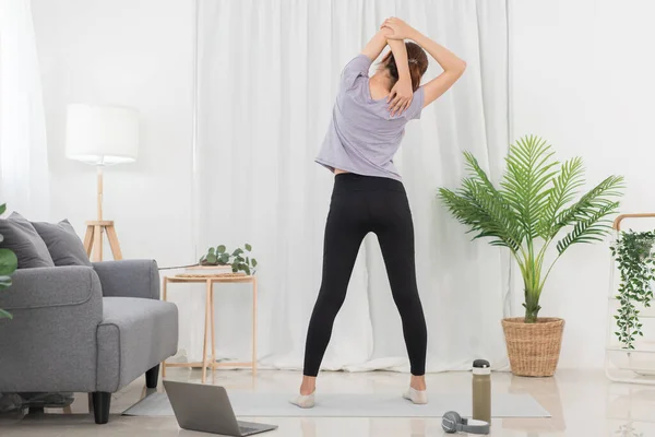 Yoga exercise concept, Young Asian woman stretching arms while doing yoga exercise online at home.