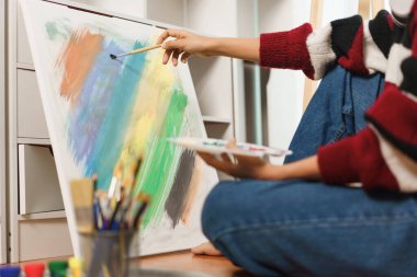 Sanat konsepti, Asyalı kadın sanatçının yere oturup tuvale boya fırçası sürmesi..