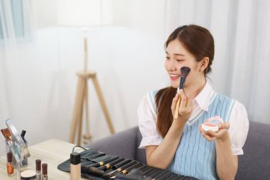 Beauty blogger concept, Asian woman apply blush on cheek to review makeup product in live streaming.