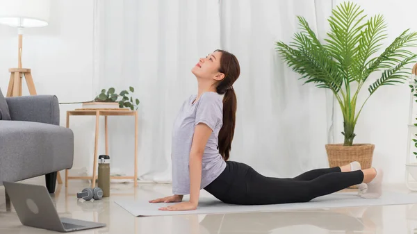 Yoga exercise concept, Asian woman doing yoga with lying in cobra pose and watching tutorial online.