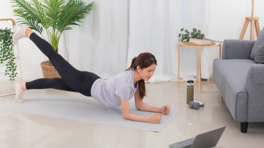 Yoga exercise concept, Young Asian woman doing plank pose and watching yoga tutorial on laptop.