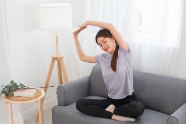 Yoga exercise concept, Young Asian woman is stretching arms while doing yoga exercise on couch.