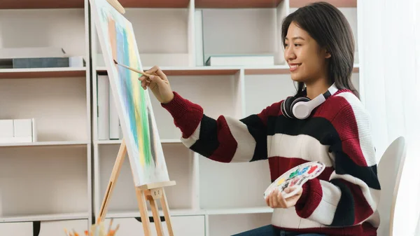 The art concept, Asian female artist using paint brush and color palette to painting on canvas.