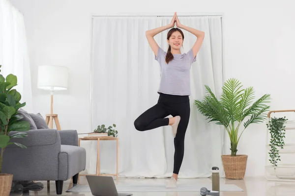 Yoga exercise concept, Asian woman standing to doing in tree pose and watching yoga tutorial online.