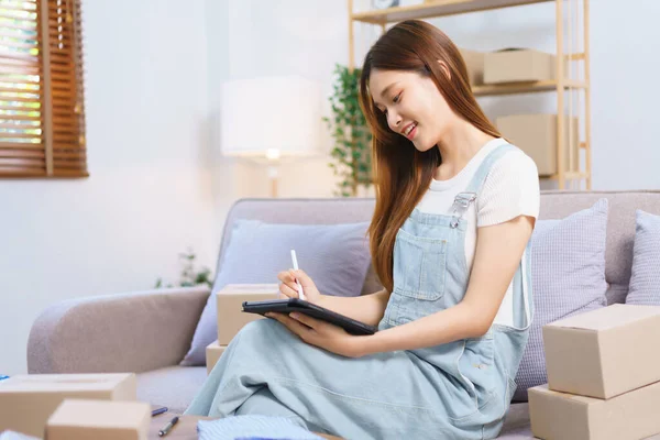 Online seller concept, Female entrepreneur checks online orders on tablet to prepare parcel boxes.