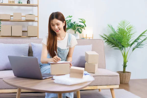 Online seller concept, Female entrepreneur read online orders on laptop to taking notes in document.