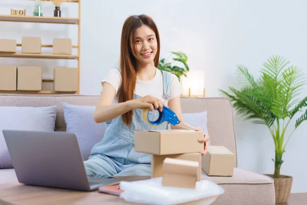 Online trader concept, Female entrepreneur is packing products and sealing parcel boxes with tape.