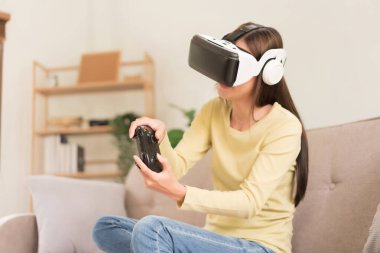 Concept of activity in home, Young woman having fun while playing game with VR glasses and joystick.