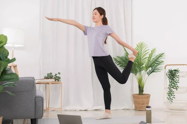 Yoga exercise concept, Young Asian woman stretching leg and arm while doing yoga exercise online.
