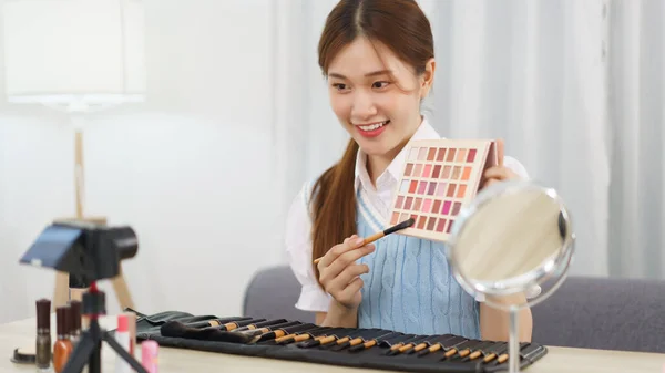 Beauty blogger concept, Asian woman use brush to applying eye shadow and review in live streaming.