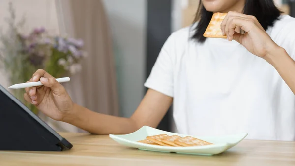 ホームライフスタイルのコンセプト タブレットを使用している若い女性と自宅で余暇中にクラッカーを食べる — ストック写真
