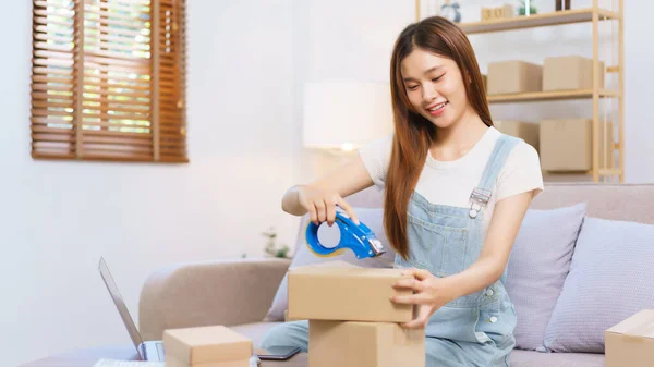 Online merchant concept, Female entrepreneur is packing products and sealing parcel boxes with tape.