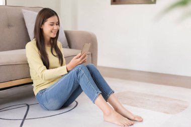 Leisure activity concept, Young woman watching movie on smartphone while sitting to relax on floor.
