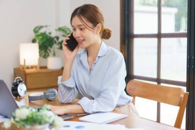 Uzak iş konsepti, iş kadını akıllı telefondan müşteriyle konuşuyor ve dizüstü bilgisayarında veri yazıyor..