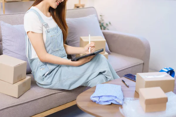 Online merchant concept, Female entrepreneur checks online orders on tablet to prepare parcel boxes.