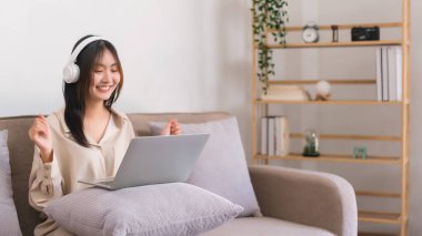 Evde rahatlama kavramı, genç Asyalı kadın film izlerken kollarını kaldırıyor ve heyecanlanıyor..