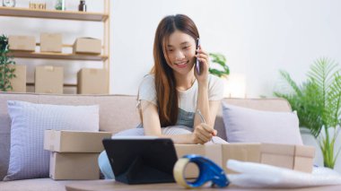 Çevrimiçi satıcı konsepti, kadın girişimci akıllı telefondan konuşur ve paket kutularına adres yazar.