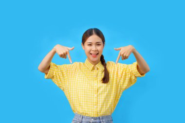 Kadınlar gülümsüyor ve işaret ediyor. Mavi arka planda izole bir şekilde gülümsüyorlar..