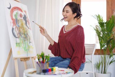 Sanat konsepti, genç Asyalı kadın resim stüdyosunda resim yapmak için boya fırçası kullanıyor..