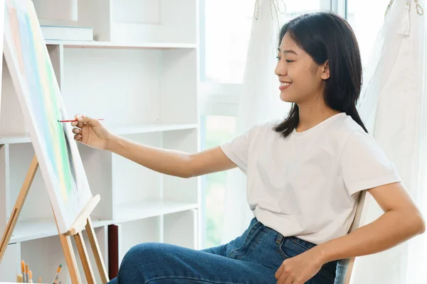 The art concept, Asian female artist use paintbrush to drawing artwork on canvas in art studio.